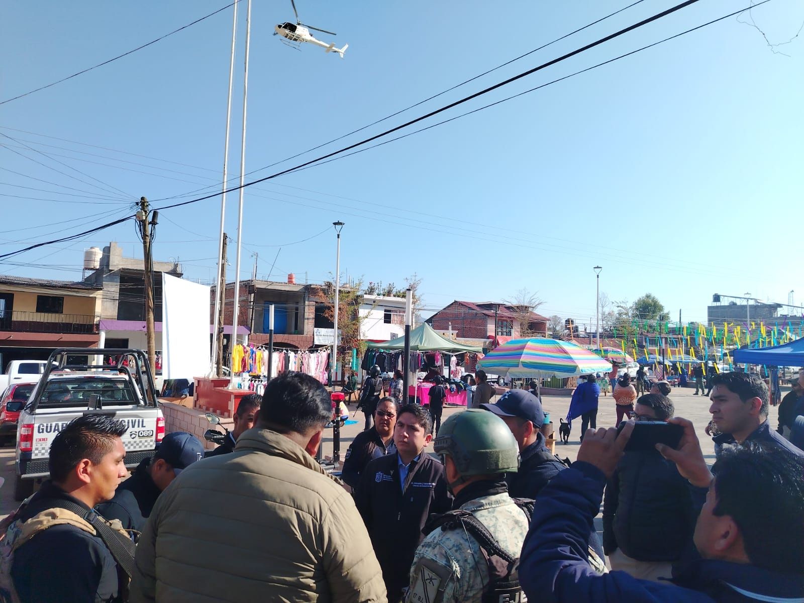 Reunión de coordinación con personal de seguridad en la plaza de una localidad, mientras un helicóptero sobrevuela la zona.