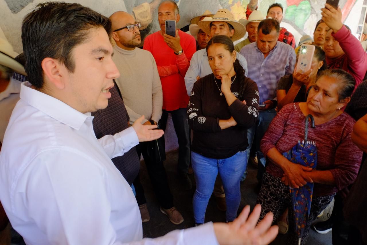 Salvador J. Vazquez Villa explica un punto a vecinas y vecinos reunidos bajo techo, frente a un mural.