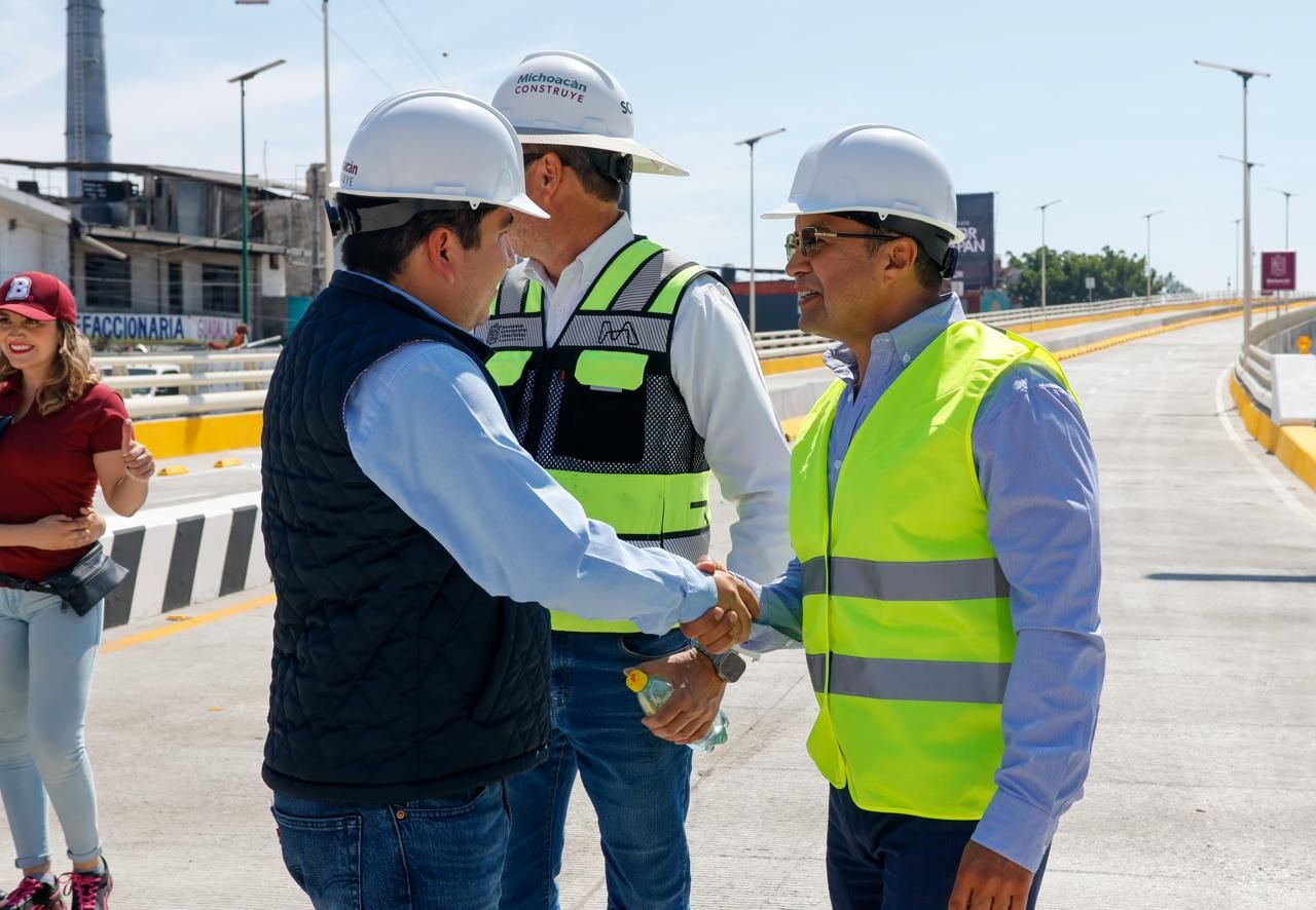 Saludo de manos entre participantes con casco y chaleco de obra durante un recorrido por un puente vehicular.
