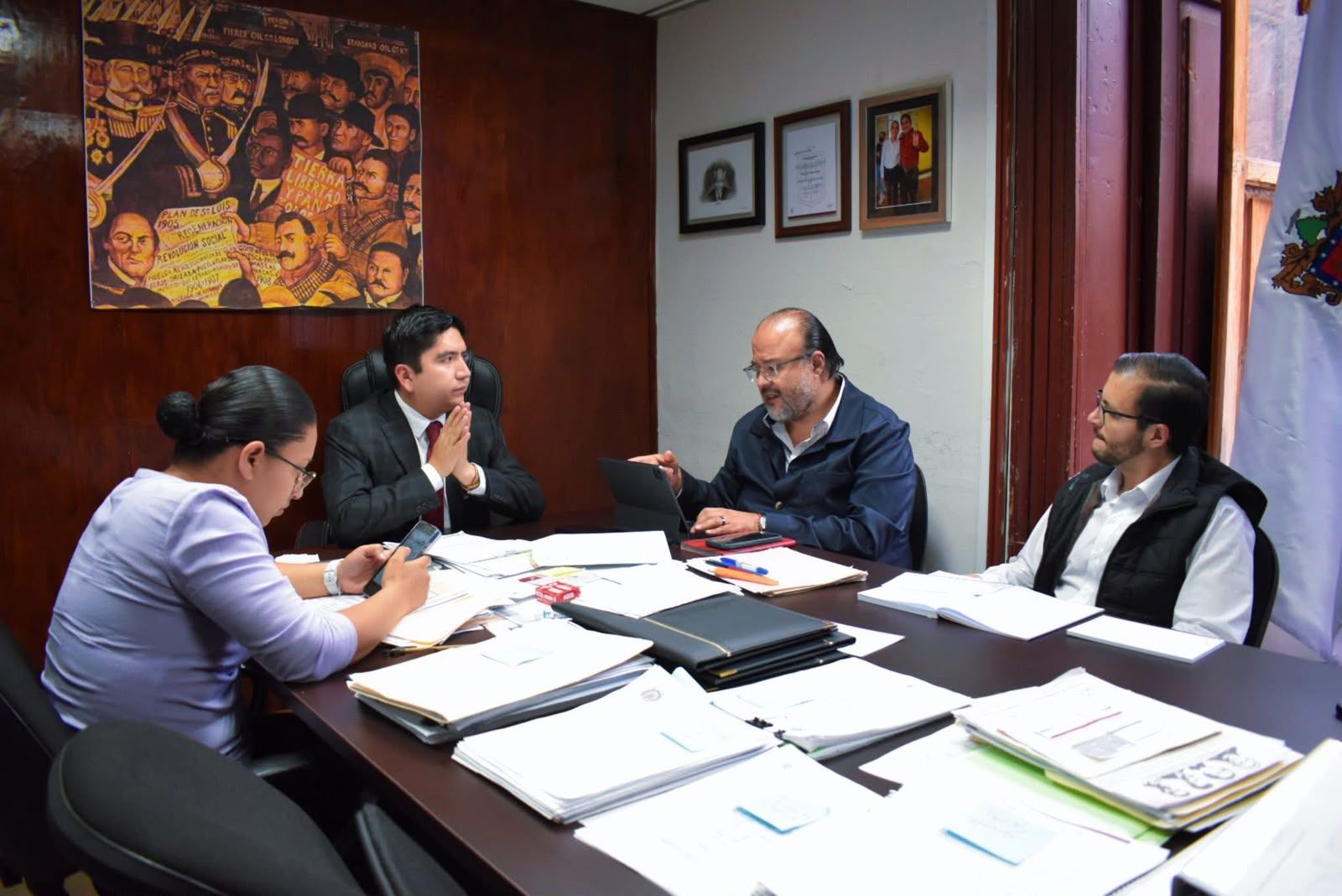 Reunión de trabajo alrededor de una mesa con expedientes y documentos abiertos.